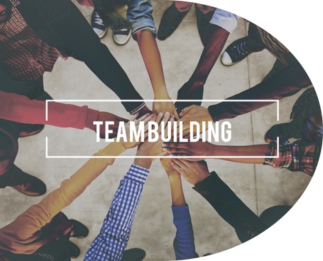 Image showing a group of people joining hands together in a circle with the word “teambuilding” added on top of it