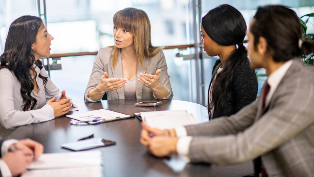 Team meeting with manager and employees. Manager is using effective communication with a team member who is questioning something.